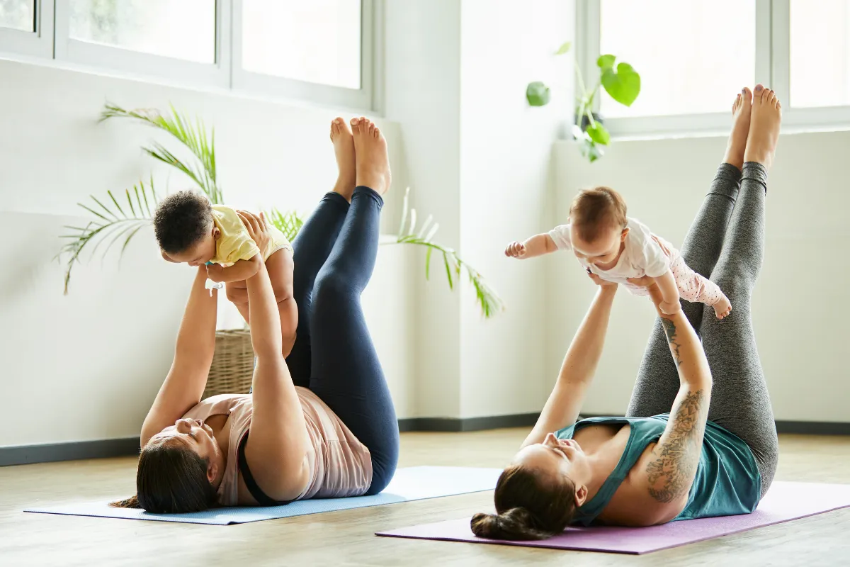 Deux mamans allongées sur leur tapis soulèvent leur bébé pendant un cours de yoga postnatal